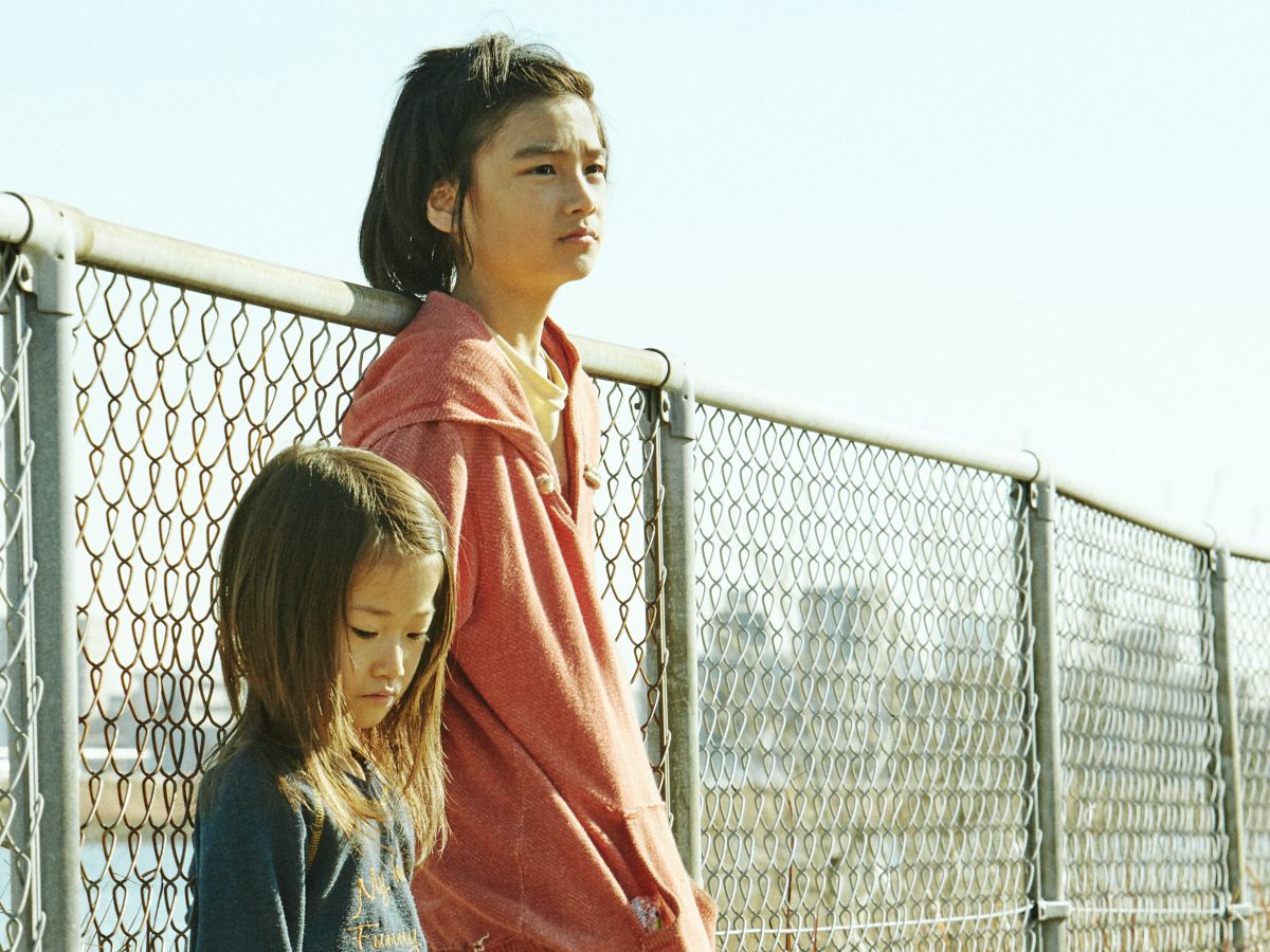 Film still: showing the two children lean against a fence
