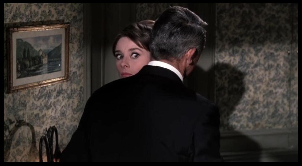 Film still showing Audrey Hepburn's character wide-eyed as she hugs Cary Grant