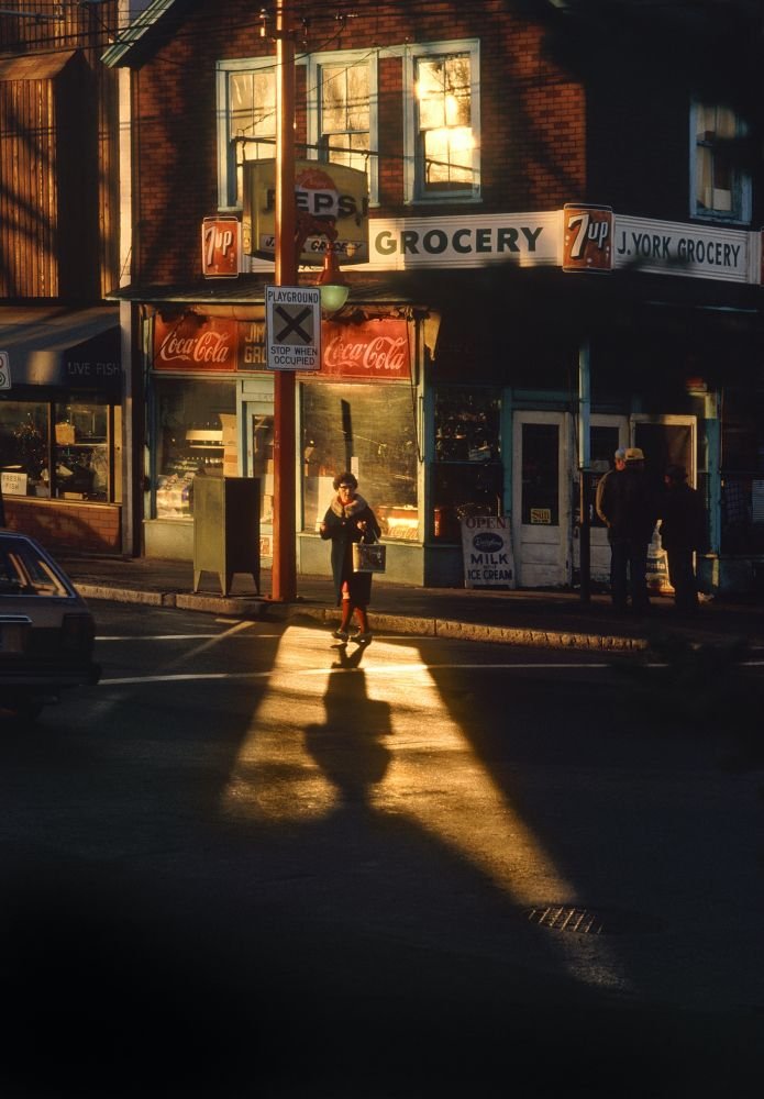 Photograph: A pedestrian crosses a street away from a corner shop.