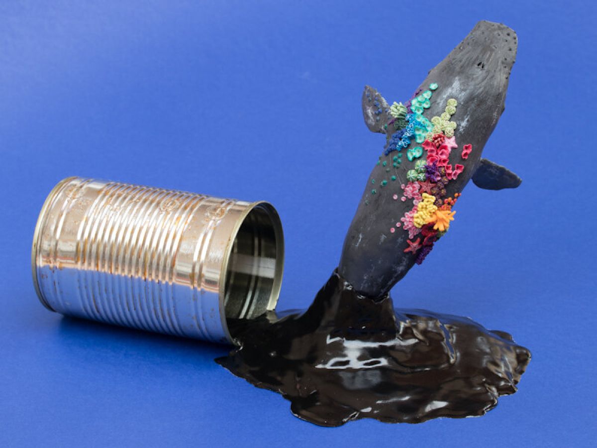 Sculpture: A tin can has tipped over, its contents – black crude oil – spill and extend outwards. Unable to escape, the blue whale jumps out from below, while its tail remains concealed within the oil. On the back of the whale is bright coloured coral.