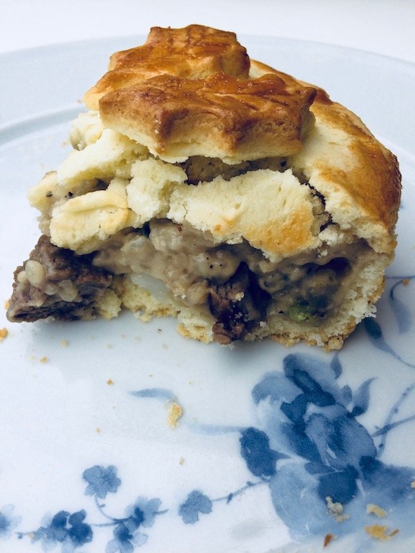 A slice of the pie showing the pastry flake away, and exposing the pie's inside with mushrooms and meat in a thick creamy sauce