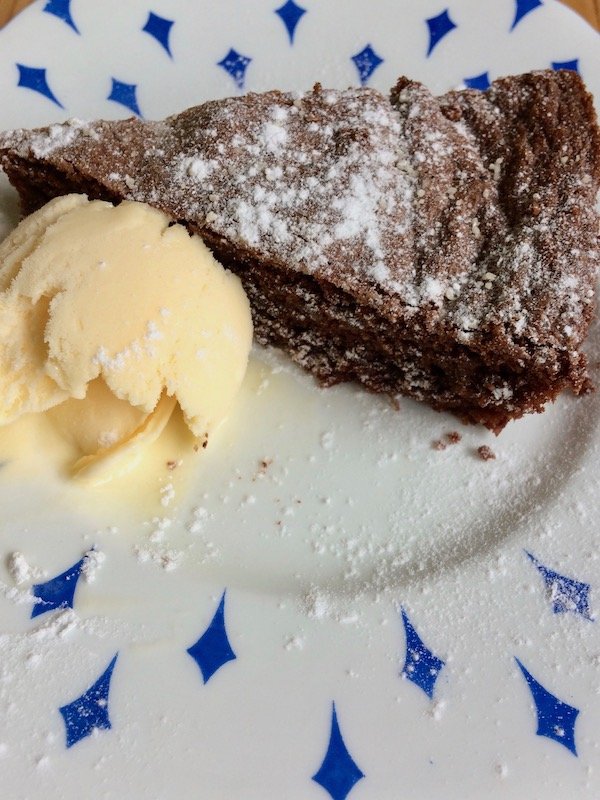 Slice of dark chocolate salted polenta cake, paired with a scoop of vanilla ice-cream