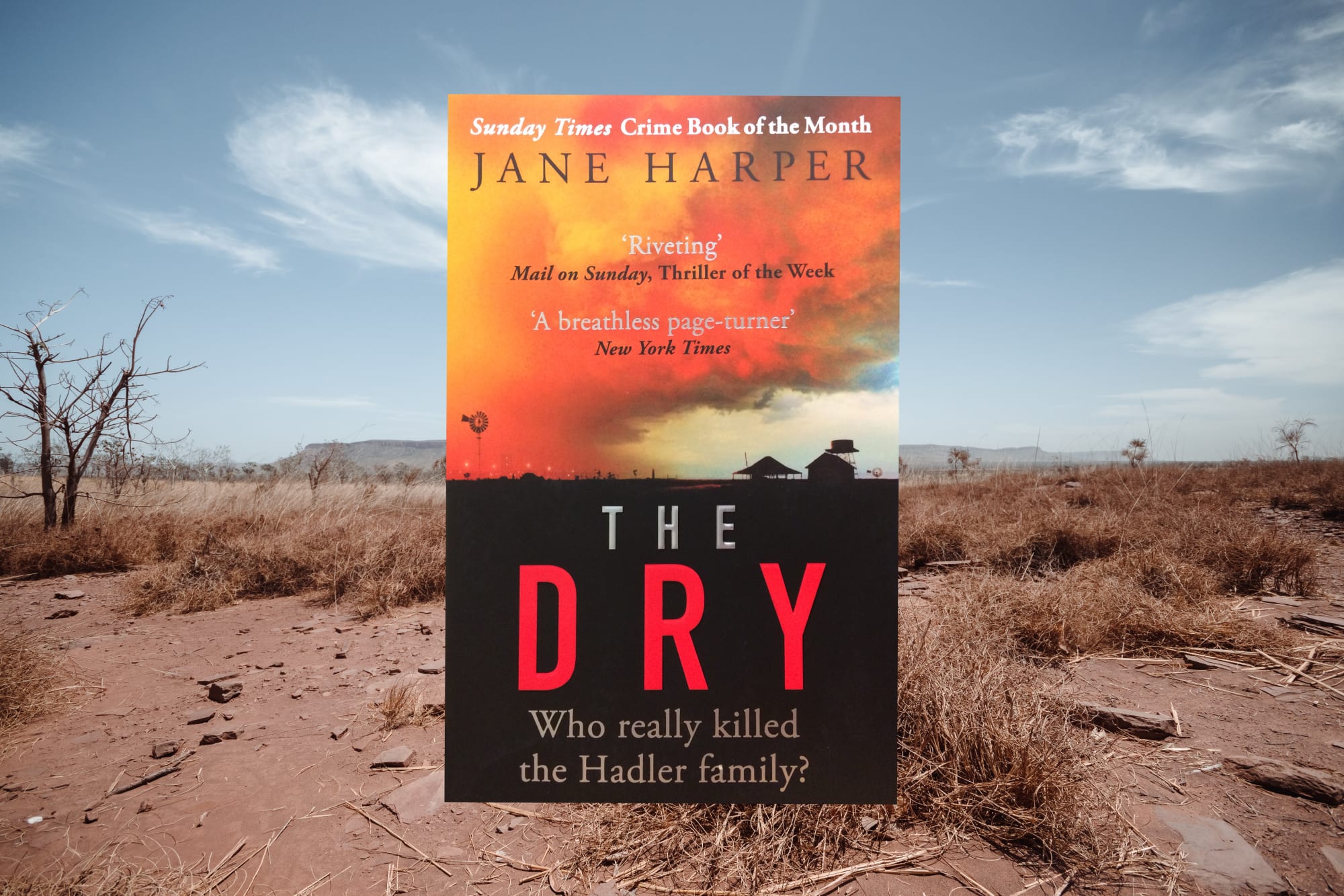 Photograph of the book's cover, which shows a barren land in shadow and a vibrant dawn above. The book is also set against a photograph of a barren and dry outback.