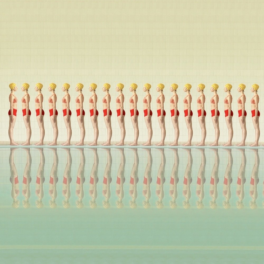 Photograph: At a swimming pool a row of women (same repeating woman) are wearing red swimsuits and yellow caps and face toward the left. At the end of this row one of the women is facing the opposite direction and is instead directly facing them.