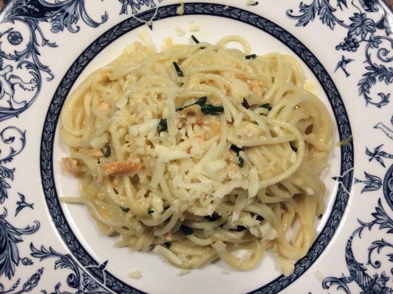 White plate with blue patterned rim, with salmon, cheddar, spaghetti and samphire with a carbonara pasta sauce