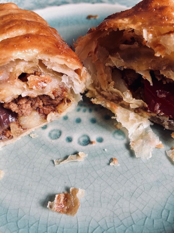 Photograph showing a spicy mince pasty cut in half, the pastry flaking at the edges.