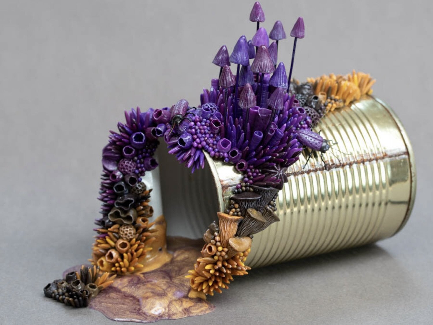 Sculpture: A tin can rests on its side, from the tin can spills toxic waste, while purple and orange fungi grow around it.